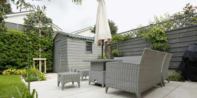 CDATA[
San Antonio homeowners spend more months of the year outdoors than almost anywhere else in the country, yet many backyards are still stuck with a slab of cracked concrete and a rusting patio set. If you have been dreaming about a covered patio, an outdoor kitchen, or a backyard that actually gets used, this guide walks you through everything: design options, materials that survive Texas heat, realistic costs, permitting, and the mistakes to avoid before you sign a contract.
At SATX Remodeling, outdoor living has become one of the fastest-growing requests we get from San Antonio homeowners, right alongside kitchen remodeling and bathroom upgrades. This guide reflects what we see working (and failing) on real projects across Bexar County.
Why San Antonio Homeowners Are Investing in Outdoor Living Spaces
San Antonio’s climate is a double-edged sword. Summers push well past 95°F, but spring, fall, and even a good chunk of winter offer ideal outdoor temperatures. Homeowners are catching on that an uncovered patio only gets used a few weeks a year, while a properly shaded, ventilated outdoor room can be used nine or ten months out of twelve.
There are three forces driving the trend locally:
- Return on investment. Realtors in the San Antonio market consistently report that finished outdoor living spaces, especially covered patios and outdoor kitchens, help homes sell faster and at a premium compared to homes with bare backyards.
- More time at home. Remote and hybrid work has made the backyard an extension of daily life rather than a weekend-only space.
- Entertaining culture. Texas hospitality runs deep, and a functional outdoor kitchen or fire pit area turns a backyard into the default gathering spot for birthdays, game days, and holidays.
If your home already shows other signs of wear, it’s worth reading our related post on the 17 signs your San Antonio home is overdue for a renovation, since outdoor spaces are often the most neglected part of an otherwise well-kept house.
Popular Types of Outdoor Living Spaces in San Antonio
Not every backyard needs the same treatment. The right project depends on lot size, how you use your yard today, and your budget. Here are the categories we build most often.
Covered Patios and Pergolas
A covered patio is usually the first phase of any outdoor living remodel, and for good reason: shade changes everything in a hot climate. Options range from a simple aluminum or wood pergola with slatted shade to a fully insulated, roofed structure with recessed lighting and ceiling fans that functions like an actual outdoor room.
Solid Roof vs. Louvered Pergola
Solid roof covers block sun and rain completely and are the better choice if you want year-round protection or plan to add a ceiling fan and lighting. Louvered (adjustable) pergolas let you control light and airflow, which many homeowners like for spring and fall days when full shade isn’t necessary.
Outdoor Kitchens
Outdoor kitchens have grown from “grill on a cart” to full kitchen builds with built-in grills, side burners, refrigeration, sinks, and stone countertops. A well-planned outdoor kitchen mirrors the same design logic as an indoor one: keep the work triangle (grill, prep, storage) tight, plan for weatherproof cabinetry, and route gas and electrical lines before the slab or pavers go down.
Fire Pits and Fireplace Features
Fire features extend usable hours into the evening and stretch the outdoor season into cooler months. Gas fire pits are popular for their instant on/off convenience and lack of smoke, while wood-burning fireplaces add a more dramatic, permanent focal point for larger patios.
Pool Decks and Lounge Areas
For homes with a pool, the deck material and layout matter as much as the pool itself. Homeowners are moving away from plain broom-finished concrete toward textured, heat-reflective surfaces (more on that below) paired with shaded lounge zones so the deck stays usable during peak summer heat.
Materials That Hold Up in San Antonio’s Climate
Texas Hill Country weather is brutal on outdoor materials: intense UV exposure, sudden hailstorms, expansive clay soil, and temperature swings between summer highs and winter freezes. Material choice is where most DIY and budget projects fail early.
Decking Materials
- Composite decking resists warping, fading, and insect damage far better than wood in our climate, though it can get hot underfoot in direct sun.
- Pressure-treated wood costs less upfront but requires re-staining or sealing every 1-2 years to handle UV exposure and occasional heavy rain.
- Tropical hardwoods like ipe offer excellent durability and a premium look but come at a higher price point.
Patio Flooring and Pavers
Concrete vs. Pavers vs. Natural Stone
Stamped or stained concrete is the most budget-friendly option and works well for simple patio slabs, but it can crack over time as clay soil shifts. Interlocking pavers cost more but are easier to repair individually if one section settles, and they handle San Antonio’s soil movement more gracefully. Natural stone, like flagstone or travertine, delivers the most upscale look and stays notably cooler underfoot than plain concrete, an important detail for a region with 100-degree summers.
Shade Structures and Roofing
Metal roofing on patio covers holds up exceptionally well against hail and UV degradation, which is one reason it has become standard on new patio builds across the area, similar to the trend we cover in our guide on metal roofing benefits for San Antonio’s climate.
Planning Your Outdoor Living Project
A good outdoor living remodel is planned with the same rigor as an interior renovation. Skipping steps here is where projects go over budget or need costly rework later.
Budget Considerations
Outdoor projects have a wide cost range because they scale with size, roof structure, and finishes. Setting a realistic budget early prevents scope creep once you start seeing design options.
Permits and HOA Requirements
Covered patios, outdoor kitchens with gas or electrical lines, and any structure over a certain footprint typically require a permit from the City of San Antonio or the relevant county building department. If you’re in a neighborhood with a homeowners association, plan on submitting your design for architectural approval before construction starts, since HOAs often regulate roof color, materials, and setback distances for backyard structures.
Timeline Expectations
A simple patio cover or paver patio can typically be completed in one to three weeks once permits are approved. A full outdoor kitchen with gas, electrical, plumbing, and custom masonry can take four to eight weeks. Weather delays are common during San Antonio’s spring storm season, so it’s smart to build in buffer time if you’re planning around an event.
Design Trends for 2026
San Antonio outdoor design is following a few clear directions this year:
- Indoor-outdoor flow using large sliding or folding glass doors that visually connect the kitchen to the patio.
- Layered lighting combining string lights, recessed can lighting, and low path lighting rather than a single bright fixture.
- Natural, textured materials like travertine, wood-look tile, and stacked stone replacing plain stamped concrete.
- Multi-zone backyards that separate a cooking/dining zone from a lounge or fire pit zone rather than one big open slab.
- Smart outdoor tech, including app-controlled lighting, misting systems, and outdoor speakers built into the design from day one.
How SATX Remodeling Approaches Outdoor Living Projects
Every outdoor living project we build follows the same structured process we use across kitchen, bathroom, and full home renovations, which you can read about in detail in our post on how SATX Remodeling manages a full renovation from start to finish. In short, that means an on-site consultation, a detailed design and material walkthrough, transparent pricing before any work begins, and a dedicated project lead who keeps you updated through permitting, construction, and final walkthrough.
Because outdoor structures tie directly into your home’s foundation, drainage, and sometimes its electrical panel, we treat these projects with the same code compliance standards as an interior remodel, not as a weekend add-on.
Cost of Outdoor Living Remodeling in San Antonio
Every backyard is different, but here is the general range homeowners in the San Antonio area typically see, based on scope and finish level:
- Basic paver or stamped concrete patio (no cover): entry-level pricing, ideal for homeowners who want a clean, usable surface without a structure.
- Covered patio with pergola or solid roof: mid-range pricing depending on roof type, size, and whether electrical and fans are added.
- Outdoor kitchen (built-in grill, counters, storage): higher pricing that scales quickly with appliance selection and countertop material.
- Full outdoor living package (cover, kitchen, fire feature, lighting): the top end of the range, comparable to a mid-size kitchen remodel, but delivered as one cohesive backyard transformation.
Because pricing depends heavily on materials, structure size, and site conditions like slope and drainage, we recommend a free on-site estimate rather than relying on national averages, which rarely reflect San Antonio labor and material costs.
Common Mistakes to Avoid
- Skipping the permit process. Unpermitted structures can complicate a future home sale and may need to be removed or reworked.
- Ignoring drainage. A beautiful patio that pools water after every rain will crack, stain, and eventually need costly repair.
- Undersizing the gas and electrical rough-in. Adding a future upgrade (a second burner, more outlets, string lighting) is far cheaper during construction than after the slab is poured.
- Choosing style over climate performance. A gorgeous material that fades, cracks, or becomes too hot to walk on barefoot within two summers isn’t a good long-term investment.
- Hiring based on price alone. The same logic that applies when choosing the best remodeling company in San Antonio applies here: the cheapest bid often means corners cut on permits, materials, or structural support.
Frequently Asked Questions
How much does a covered patio cost in San Antonio?
Cost depends mainly on size, roof type (louvered pergola vs. solid insulated roof), and whether you add electrical, lighting, or ceiling fans. A basic pergola-style cover costs less than a fully roofed, insulated structure with built-in lighting and fans.
Do I need a permit to build an outdoor kitchen in San Antonio?
In most cases, yes. Any structure that involves gas lines, electrical wiring, plumbing, or a permanent roof typically requires a permit from the local building department. A licensed remodeling contractor will handle this as part of the project.
What is the best patio flooring for hot Texas summers?
Natural stone like travertine and light-colored pavers stay noticeably cooler underfoot than plain concrete, making them a better choice for pool decks and uncovered patio areas that get direct sun exposure.
How long does an outdoor living remodel take?
A simple patio or paver project can take one to three weeks after permit approval. A full outdoor kitchen and covered patio combination typically takes four to eight weeks, depending on structural complexity and weather.
Can an outdoor kitchen increase my home’s resale value?
Yes. Well-built outdoor kitchens and covered patios are consistently cited by San Antonio real estate agents as features that help homes stand out and sell faster, particularly in a market where outdoor living is used most of the year.
Should I build a fire pit or a fireplace?
A fire pit works well for casual, flexible seating and is generally less expensive. A fireplace creates a stronger visual focal point and works better as an anchor for a larger, more formal patio layout. Many homeowners choose gas over wood-burning for convenience and lower maintenance.
Ready to Plan Your Backyard Remodel?
Whether you’re picturing a simple shaded patio or a full outdoor kitchen and entertaining space, the SATX Remodeling team can walk your property, talk through layout options, and give you a clear, honest estimate before any work begins. If you’re also considering updates inside the home, take a look at our guides on kitchen and bathroom remodeling in San Antonio or our overview of what to expect from a home remodel from start to finish. Reach out today to schedule your free outdoor living consultation.
![Covered patio and outdoor living space remodel in San Antonio with table and seating